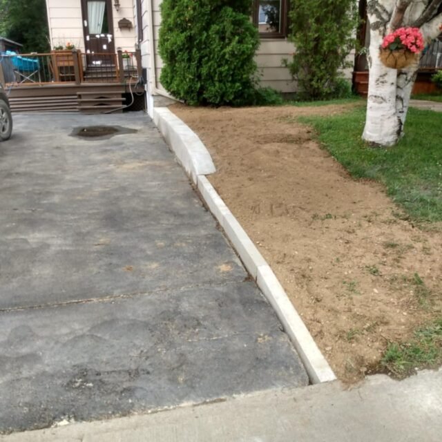 Muret en béton séparant un stationnement d'une pelouse.